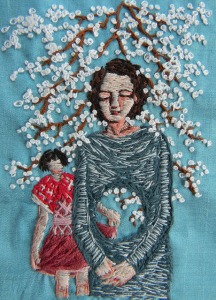 An embroidered image of a middle-aged woman standing with her eyes closed and hands folded. There is a large circular hole in her middle, through which you can see a smaller, younger girl in the background. Tree branches covered with white blossoms frame the woman's head and shoulders.