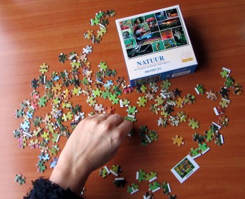 A slim hand moves jigsaw puzzle pieces laid out on a table.